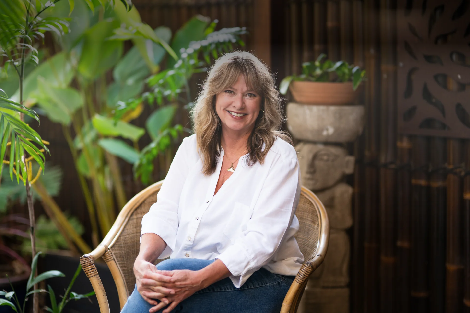 Kimberley sitting outside on a cane chair, plants and wooden wall in the background.