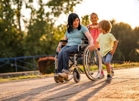 A smiling woman in a wheelchair is accompanied by two young children