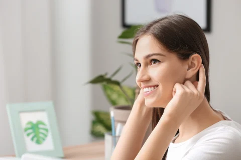 A smiling young woman testing her hearing aid.