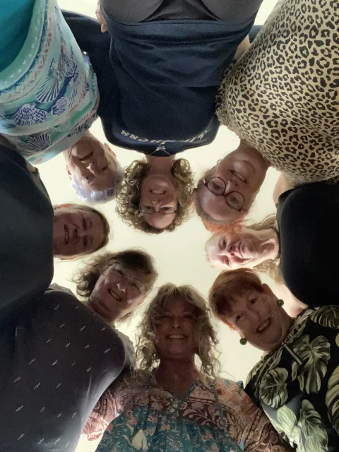 A group of people in a circle looking down at the camera.